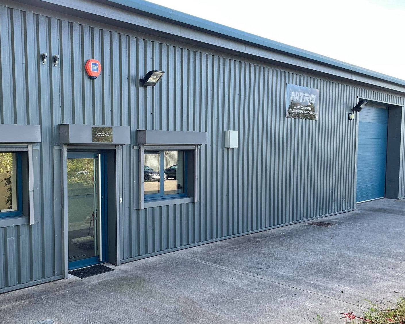 A gray corrugated metal industrial building with a blue garage door, blue entry door, windows, and a visible NITRO sign on the exterior wall.