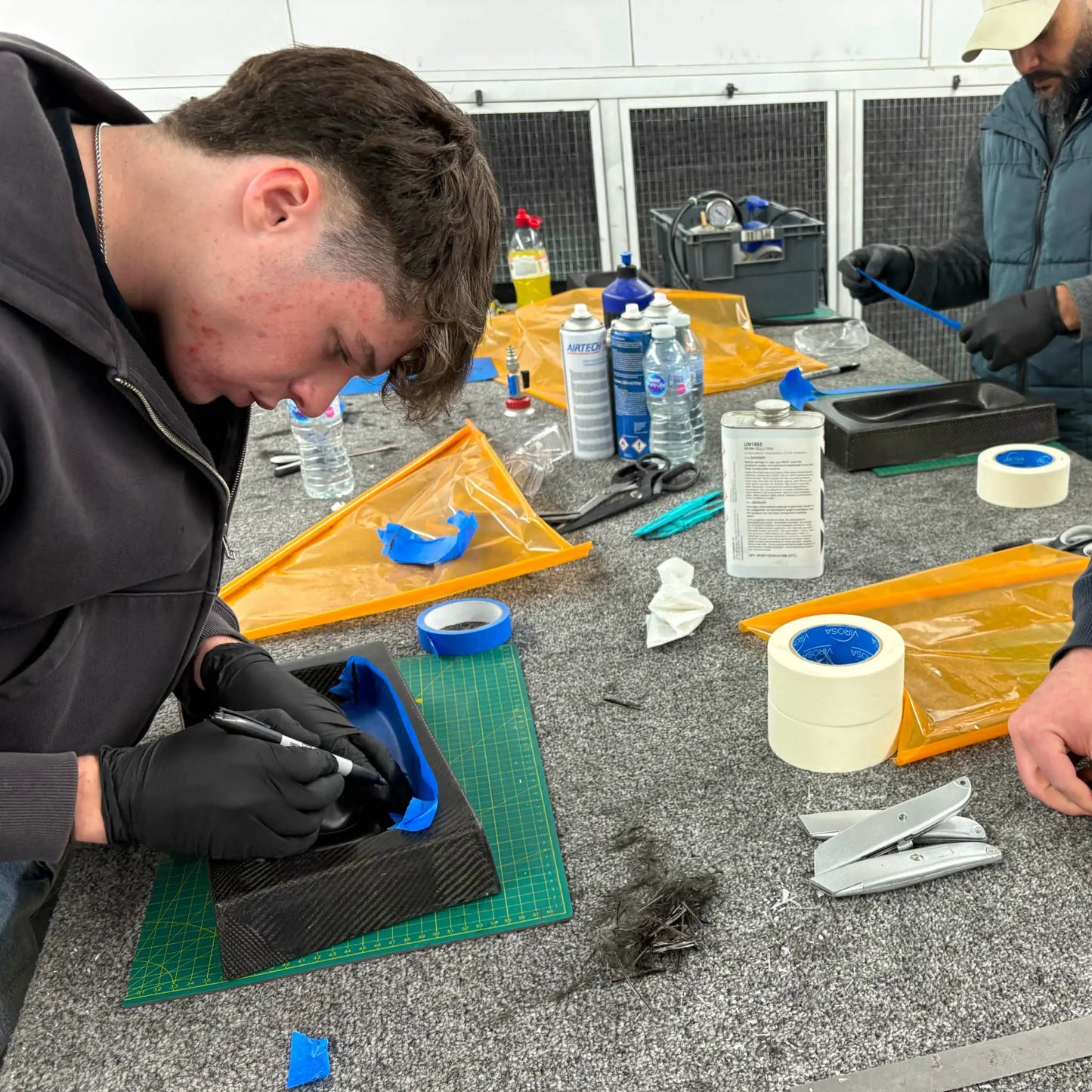 Prepreg carbon fibre lay-up demonstration on a composites training course, showing detailed hand placement and material control.